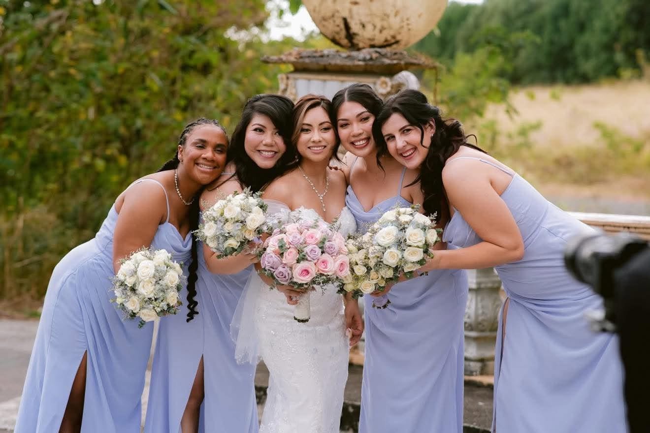 Bride and her bridesmaids in lavender gowns, smiling together for a wedding portrait.